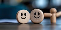 Wooden round faces with happy smiles and blurred figure in background represent positive emotions, friendship and social connections on dark surface.