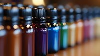 Small glass bottles with colorful liquids arranged in row showing purple, blue and other vibrant tones against blurred bokeh background, macro photography for aromatherapy concept.