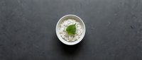Green matcha latte with foam art in white ceramic cup on dark slate surface, top view of hot beverage with leaf design for cafe menu and food photography.