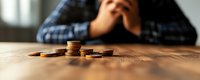 Stressed man with head in hands looking at small pile of coins on table representing financial hardship and money problems.