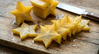 Fresh yellow star fruit slices on rustic wooden cutting board with knife, tropical exotic carambola ready for healthy snacking and culinary preparation.