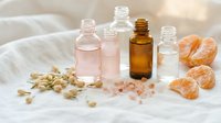 Natural skincare essential oils in glass bottles with citrus fruits and sea salt on white fabric background for aromatherapy and wellness treatments.