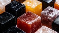Colorful sugar coated gummy candy cubes in black, orange, red and pink colors arranged in rows on dark background, macro food photography for confectionery.