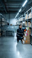 Warehouse worker organizing packages in modern distribution center with conveyor system and industrial shelving for logistics operations.