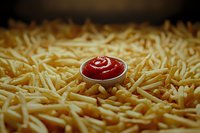 Small red sauce bowl nestled in golden french fries creating contrast and appetizing composition for restaurant menu design and food marketing.