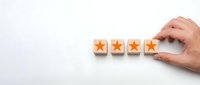 Hand placing wooden blocks with orange stars for customer rating and feedback system on white background.