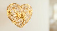 Golden wire heart-shaped decoration with warm LED lights glowing against soft blurred background for romantic occasions and festive celebrations.