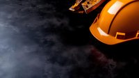 Orange construction hard hat and measuring tools on dark concrete background with copy space for construction industry and safety concept.