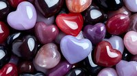 Colorful polished gemstone hearts in various shades of red, purple, pink, and black, arranged together to create a romantic backdrop.