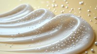 Creamy white cosmetic texture with flowing waves and sparkling droplets on golden background for skincare and beauty product advertising.