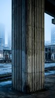 Weathered concrete column in abandoned industrial building with urban skyline backdrop showcasing decay and architectural brutalism elements.