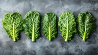 Fresh kale leaves arranged in row on dark stone background, showcasing vibrant green color and textured surfaces for healthy cooking inspiration.