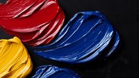 Vibrant oil paint strokes in primary colors red, blue and yellow on black background create bold artistic texture. Abstract creative palette knife technique shows rich pigments.