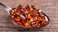Amber fish oil omega-3 gel capsules on vintage metal spoon against rustic wooden background, nutritional supplement and vitamin concept for health.