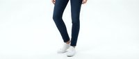 Woman wearing dark navy blue skinny jeans and white sneakers standing against white background, showcasing casual everyday fashion and footwear styling.
