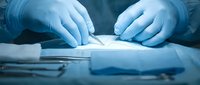 Surgeon hands in sterile gloves performing precise medical procedure with surgical instruments in operating room under bright clinical lighting.