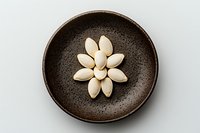 White pumpkin seeds arranged in flower shape pattern on rustic brown ceramic plate against light background, overhead view for food styling and design.