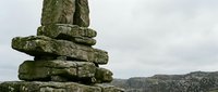 Ancient stone cairn stack against mountain landscape with cloudy sky. Weathered rock pile marker for hiking trails and outdoor navigation adventures.
