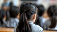 Young Asian female student with ponytail sitting in crowded classroom, rear view showing dark hair and grey uniform, focus on back of head in educational setting.