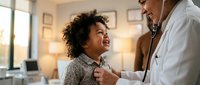 Young African American boy smiling during pediatric checkup with male doctor using stethoscope in bright medical office for healthcare examination.