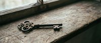 Antique rusty skeleton key resting on a weathered wooden windowsill, evoking mystery, history, and forgotten secrets in a moody vintage setting.