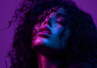 Young African American woman with curly hair in dramatic neon pink and blue lighting against purple background, eyes closed in artistic portrait expressing emotion.