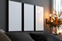 Three blank white vertical frames mockup on dark gray wall with warm lighting and autumn floral decoration, modern interior design background.