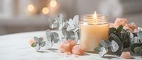 Relaxing spa atmosphere with burning candle, eucalyptus branches and rose quartz crystals on white surface. Wellness meditation aromatherapy home decor setup.