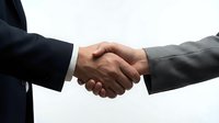 Professional business handshake between two executives in formal suits representing partnership, agreement, and successful deal completion in corporate environment.