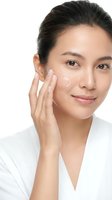 Young Asian woman applying facial cream moisturizer to cheek with gentle touch, skincare routine and beauty treatment on white background.