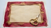 Vintage burgundy velvet frame with aged parchment center and ornate gold scissors on crafting surface for antique design projects.