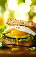 Breakfast sandwich with runny egg yolk, avocado and toast on green bokeh background, perfect for healthy morning meal options.