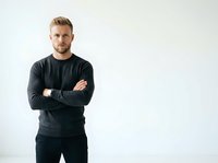 Caucasian male with blonde hair and beard wearing black long-sleeve shirt, arms crossed, standing against white background for portrait and professional use.