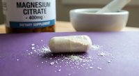 Magnesium citrate supplement capsule opened with white powder spilling on purple surface next to mortar and pestle for health and wellness concepts.