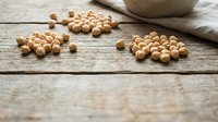 Scattered chickpeas on rustic wooden surface with ceramic bowl, suitable for food photography, cooking blogs, nutrition content, and healthy eating publications.