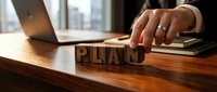Business professional arranging wooden letter blocks spelling PLAN on office desk with laptop and cityscape background for strategic planning concepts.
