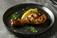 Grilled chicken leg with crispy golden-brown skin garnished with fresh herbs on black plate. Dark moody food photography with selective lighting.