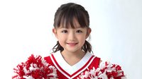 Young Asian girl in red and white cheerleader uniform with pom-poms, smiling at camera against white background.