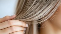 Closeup of woman's hand gently holding smooth blonde hair strands against blurred skin background, demonstrating healthy, straight hair texture and haircare concept.