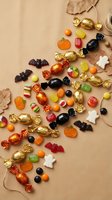 Assorted Halloween candies scattered on beige background with autumn leaves and twine for seasonal celebration and trick or treat festivities.