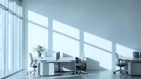 Modern minimalist office interior with natural light streaming through large windows creating geometric shadows on white desks and ergonomic chairs.