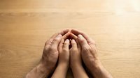 Adult and child hands forming protective circle on wooden surface symbolizing family care, protection, support and generational bond in warm natural lighting.
