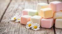 Colorful marshmallows stacked on rustic wooden background with fresh daisy flowers, creating sweet composition for confectionery and dessert concepts.
