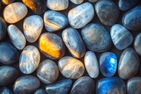 Polished moonstone and labradorite pebbles with vibrant blue and golden flashes creating mystical pattern, natural mineral texture for spiritual practices.