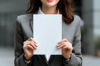 Professional businesswoman in gray suit holding blank white paper sheet for mockup presentations and corporate communications.