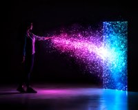 Silhouette of young man creating magical light stream with glowing pink and blue particles flowing into mysterious doorway on dark background with reflection.