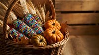 Autumn harvest basket with colorful Indian corn, mini pumpkins and wheat stalks on rustic wooden background for seasonal decoration and thanksgiving displays.