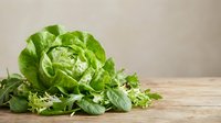 Fresh green lettuce head with mixed salad leaves on rustic wooden table against neutral background for healthy eating and organic food concepts.
