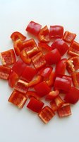 Freshly chopped red bell pepper pieces scattered on a white surface, vibrant and ready for cooking, salads, or healthy meal preparation.