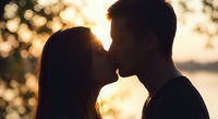 Romantic couple silhouette kissing at golden hour sunset with warm bokeh lights creating intimate atmosphere for love and relationship concepts.